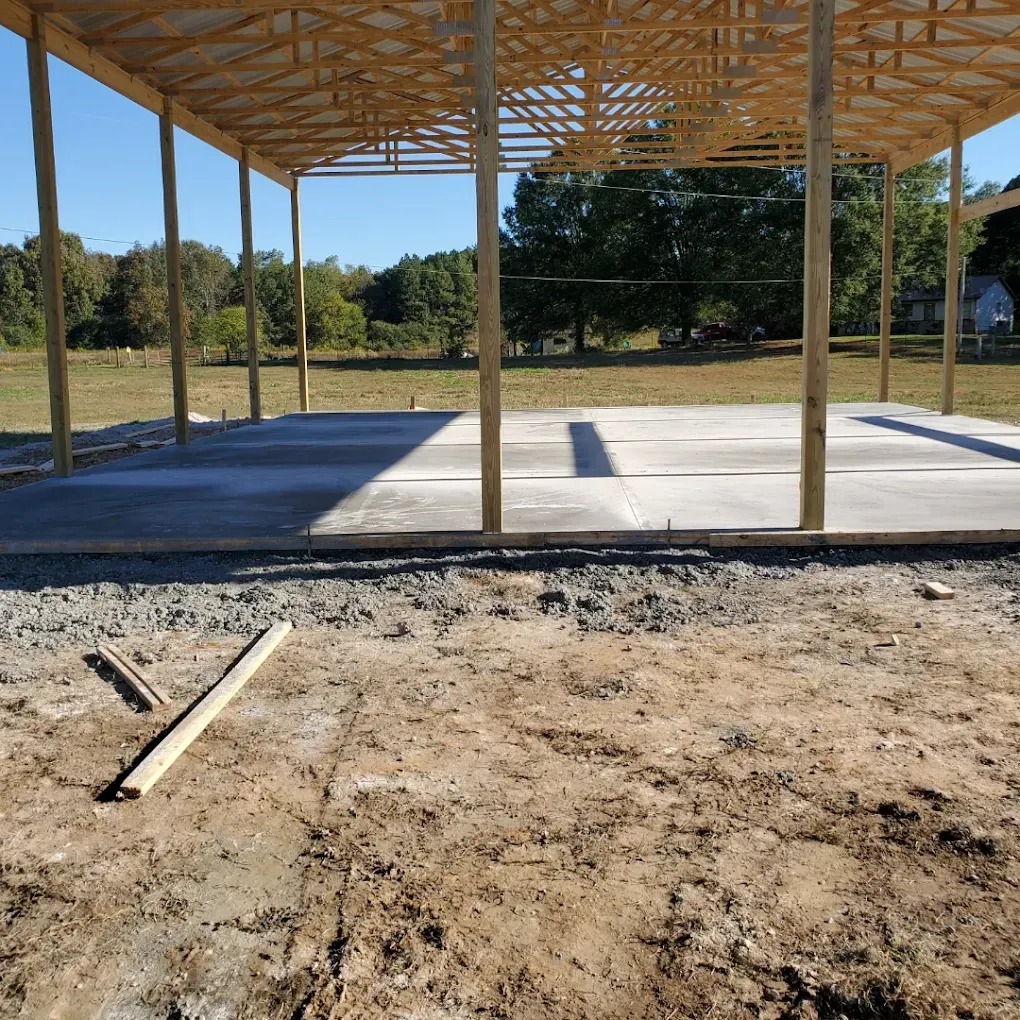 Construction site with wooden frame roof and concrete floor, outdoors.