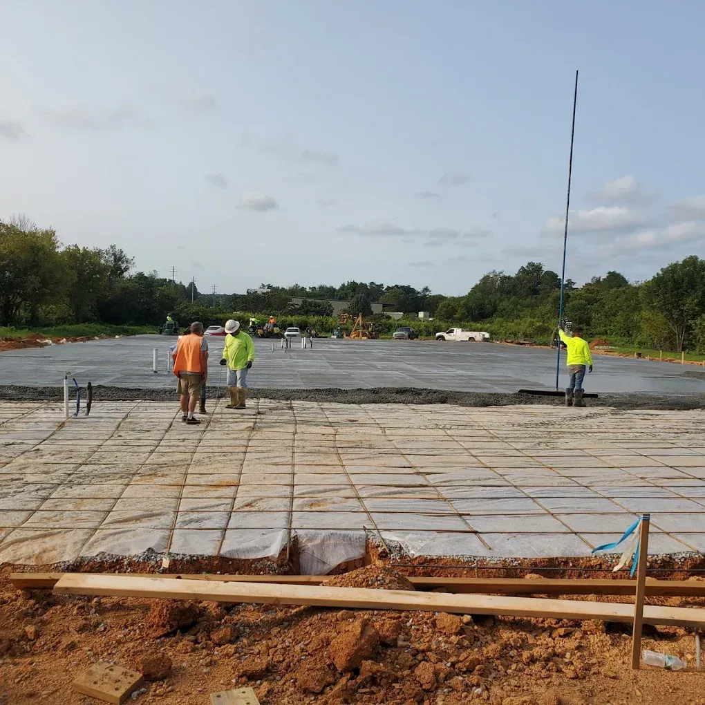 Construction workers leveling concrete on a prepared foundation; outdoor setting, overcast.