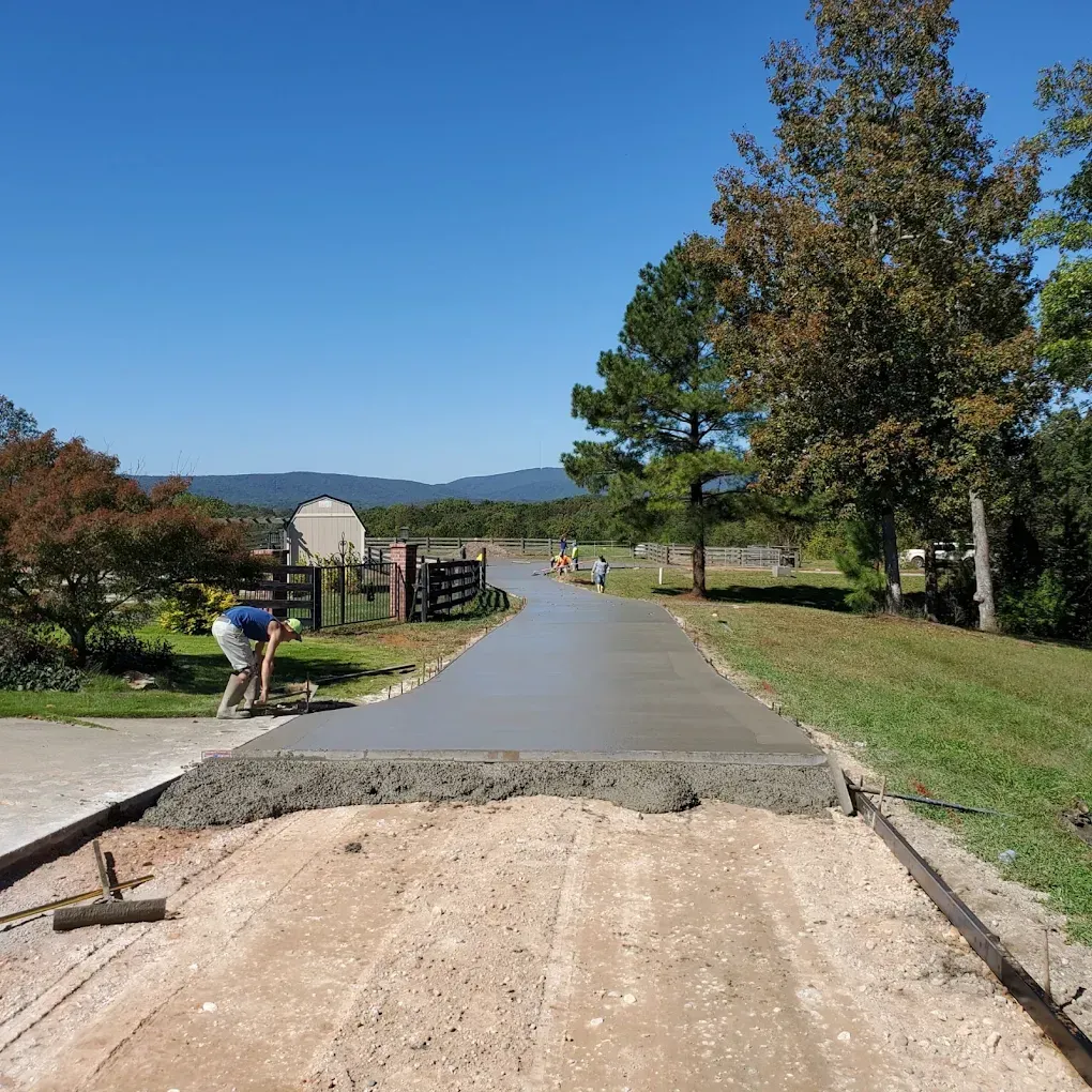 A man smoothing wet concrete on a driveway under construction in a rural setting.