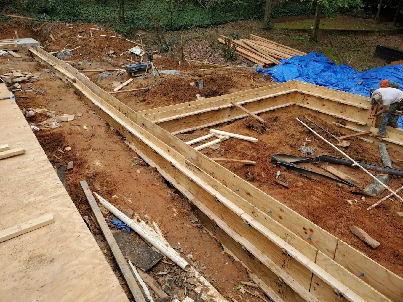 Construction site with wooden forms for foundation walls, dirt, and a worker.