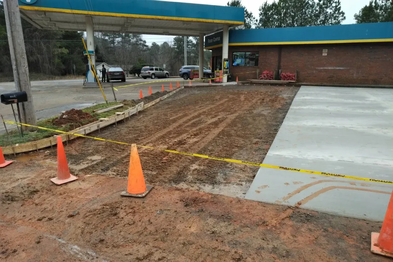 Gas station under construction; muddy ground, caution tape, orange cones, and cars.