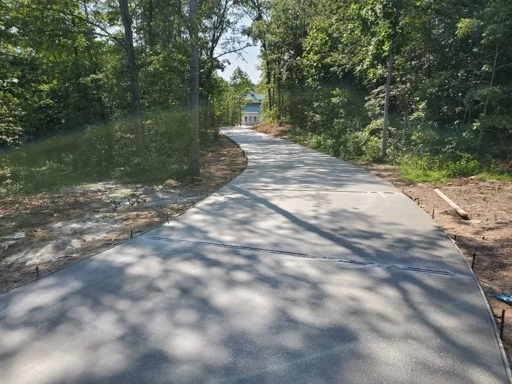 Concrete driveway curves through trees, leading to a white house in the distance.