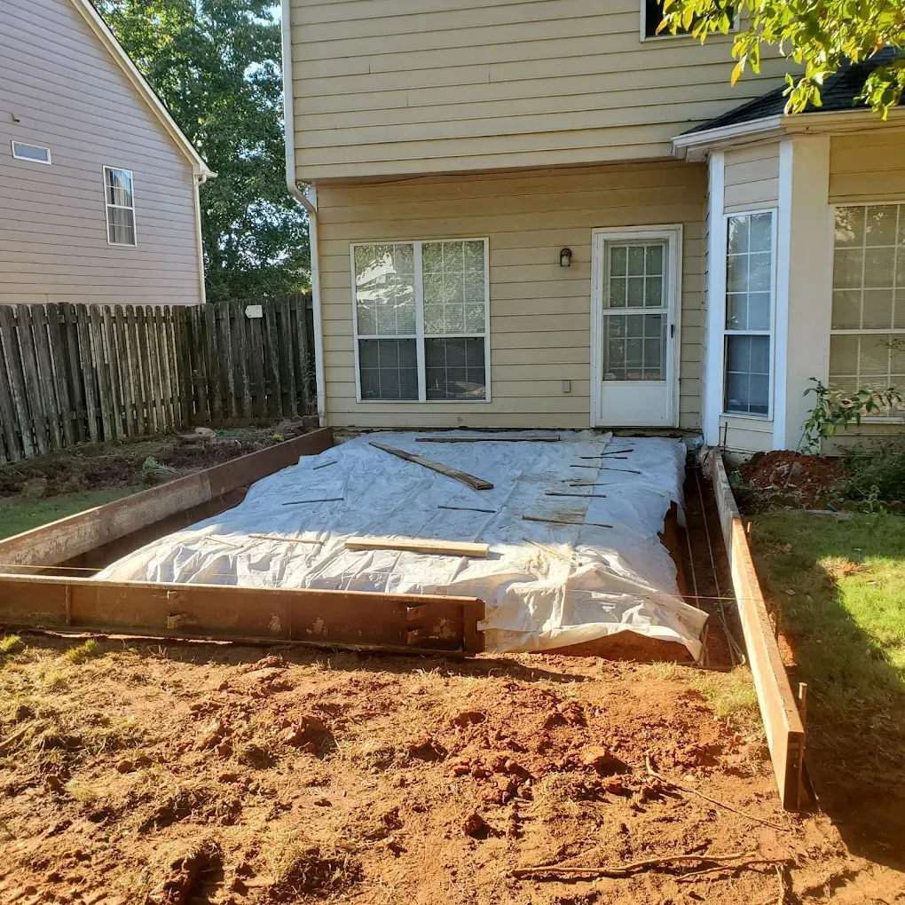 A backyard with a concrete slab in progress, bordered by wooden forms, in front of a house.