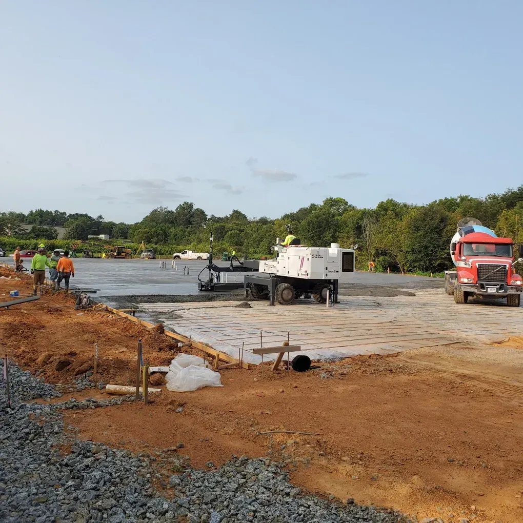 Construction site: Workers pouring concrete foundation with a red cement truck and white cement mixer.