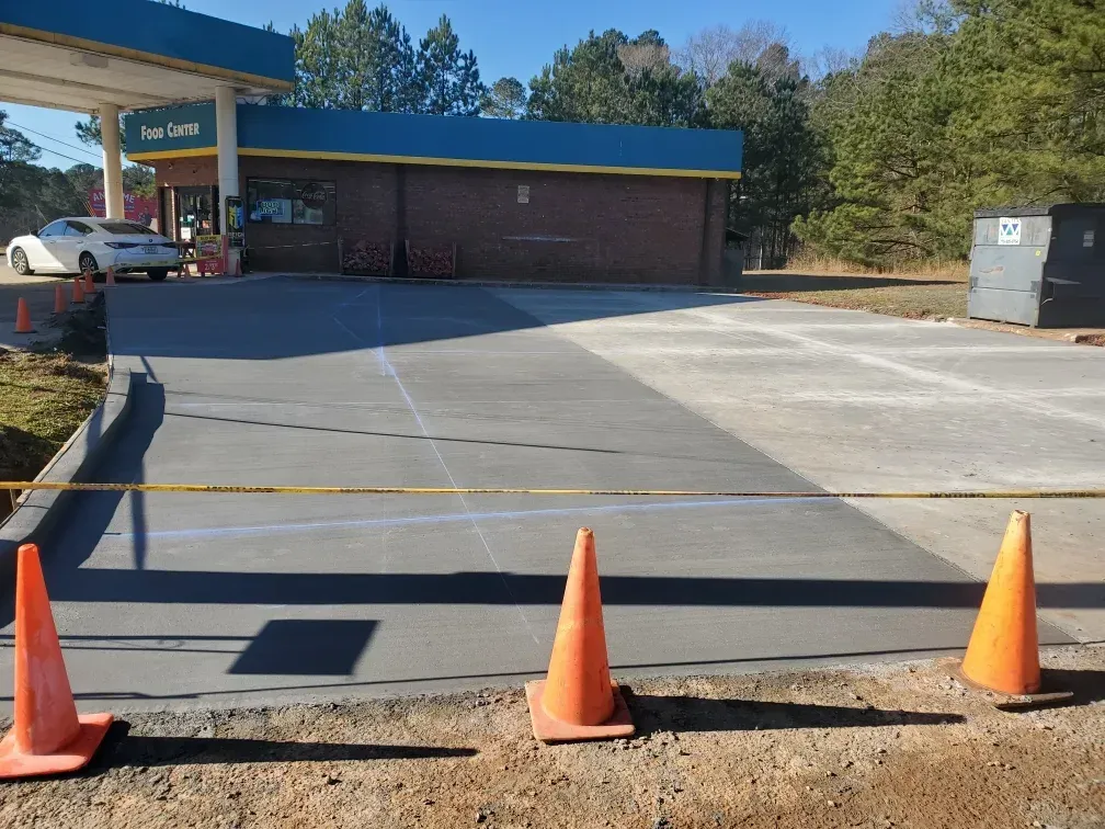 Gas station under construction with orange cones, caution tape, and freshly poured concrete.