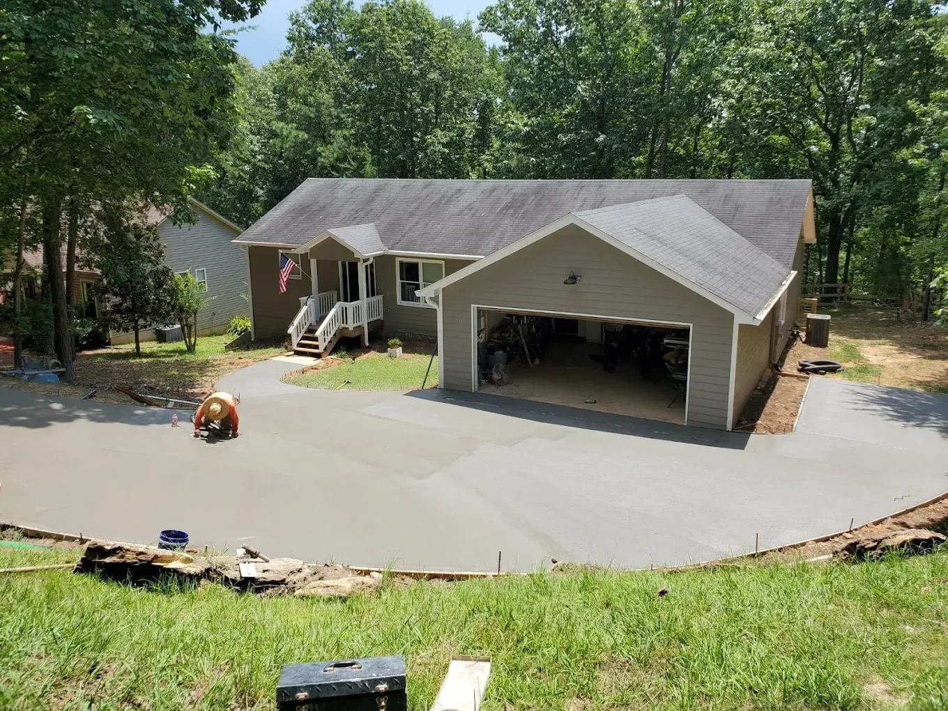 Concrete driveway being poured at a house with a garage; person working, green grass, and blue sky.