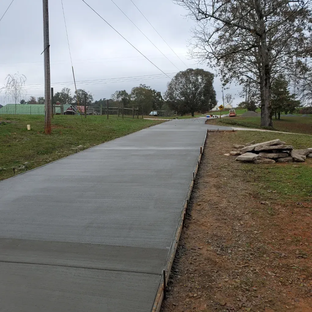 Newly poured concrete path in a grassy area with power lines and trees.