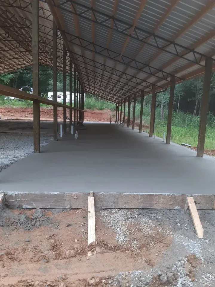 New concrete slab under a metal-roofed structure with wooden posts and a dirt foreground.
