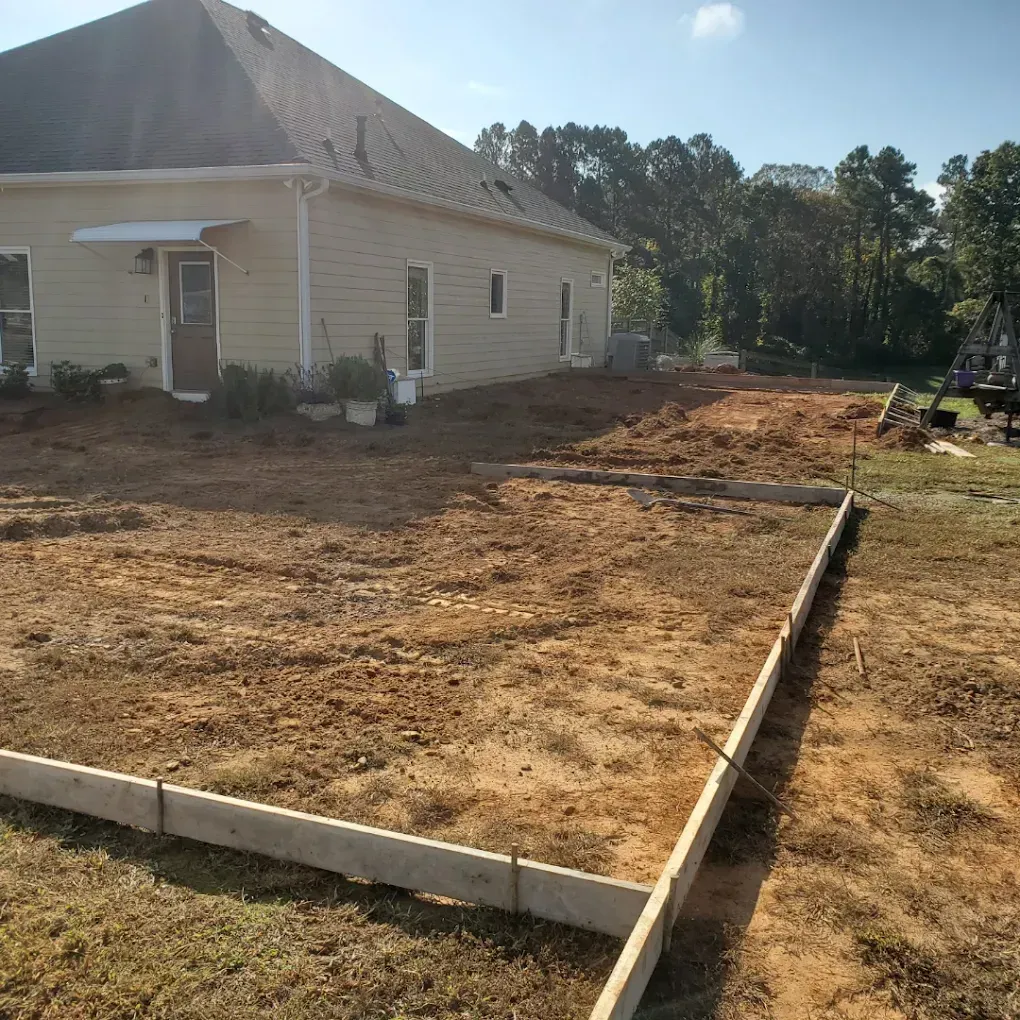 Backyard with soil and concrete forms; a house and trees in the background.