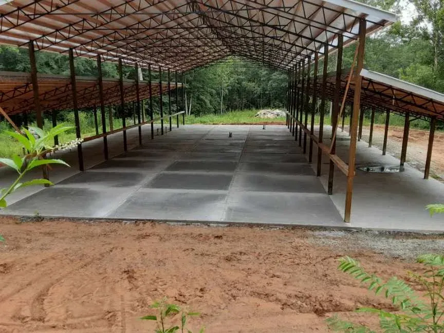 Covered concrete structure with open sides, surrounded by red dirt and trees.