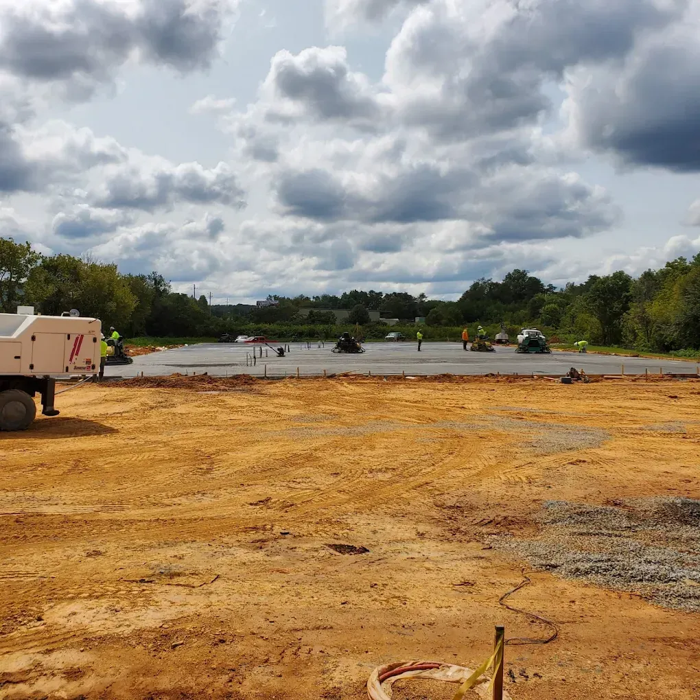 Construction site with concrete slab, workers, machinery, and cloudy sky.