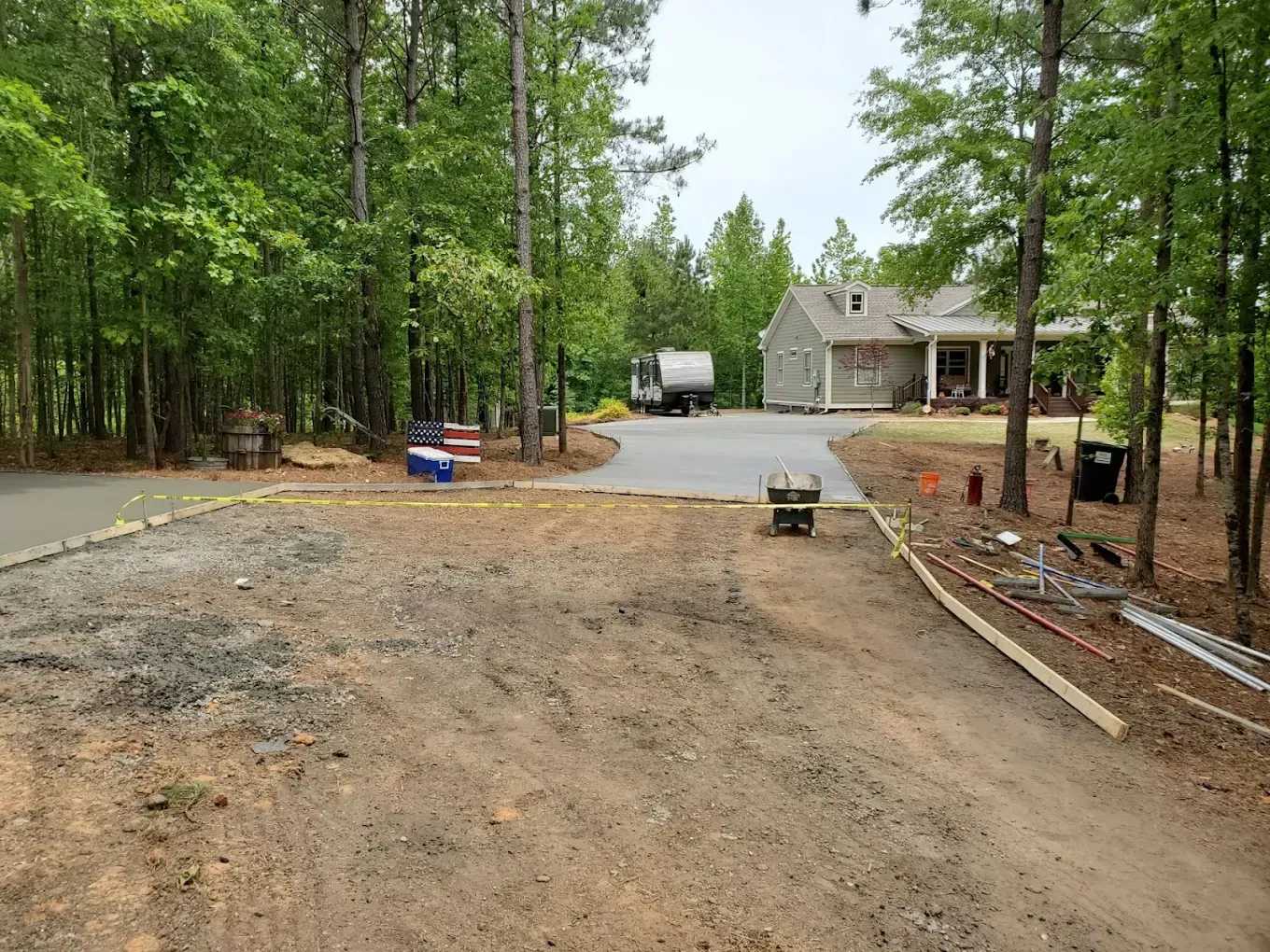 Dirt and gravel driveway leads to paved area with a house and RV. Trees surround the scene.