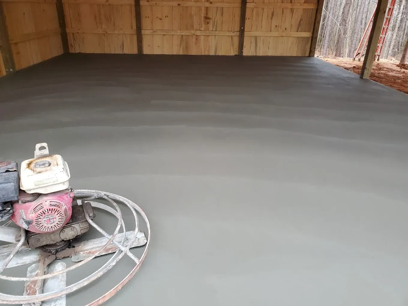 A cement floor being smoothed by a power trowel inside a wooden structure.