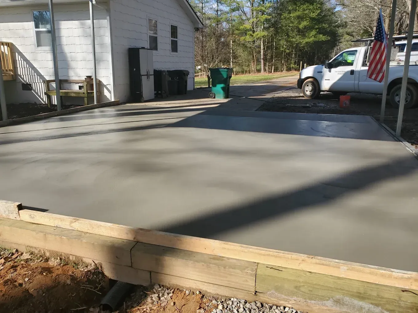 Newly poured concrete driveway next to a house, with a white truck and American flag visible.