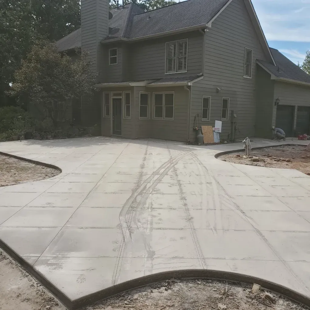 Newly poured concrete driveway in front of a two-story house, with tire tracks.
