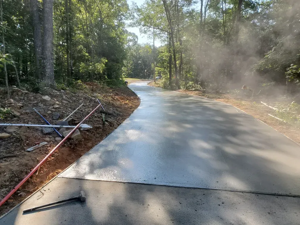 Freshly poured concrete driveway in a wooded area with morning mist.