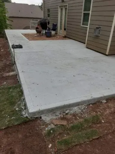 Newly poured concrete patio next to a house, with unfinished edges and adjacent grass.