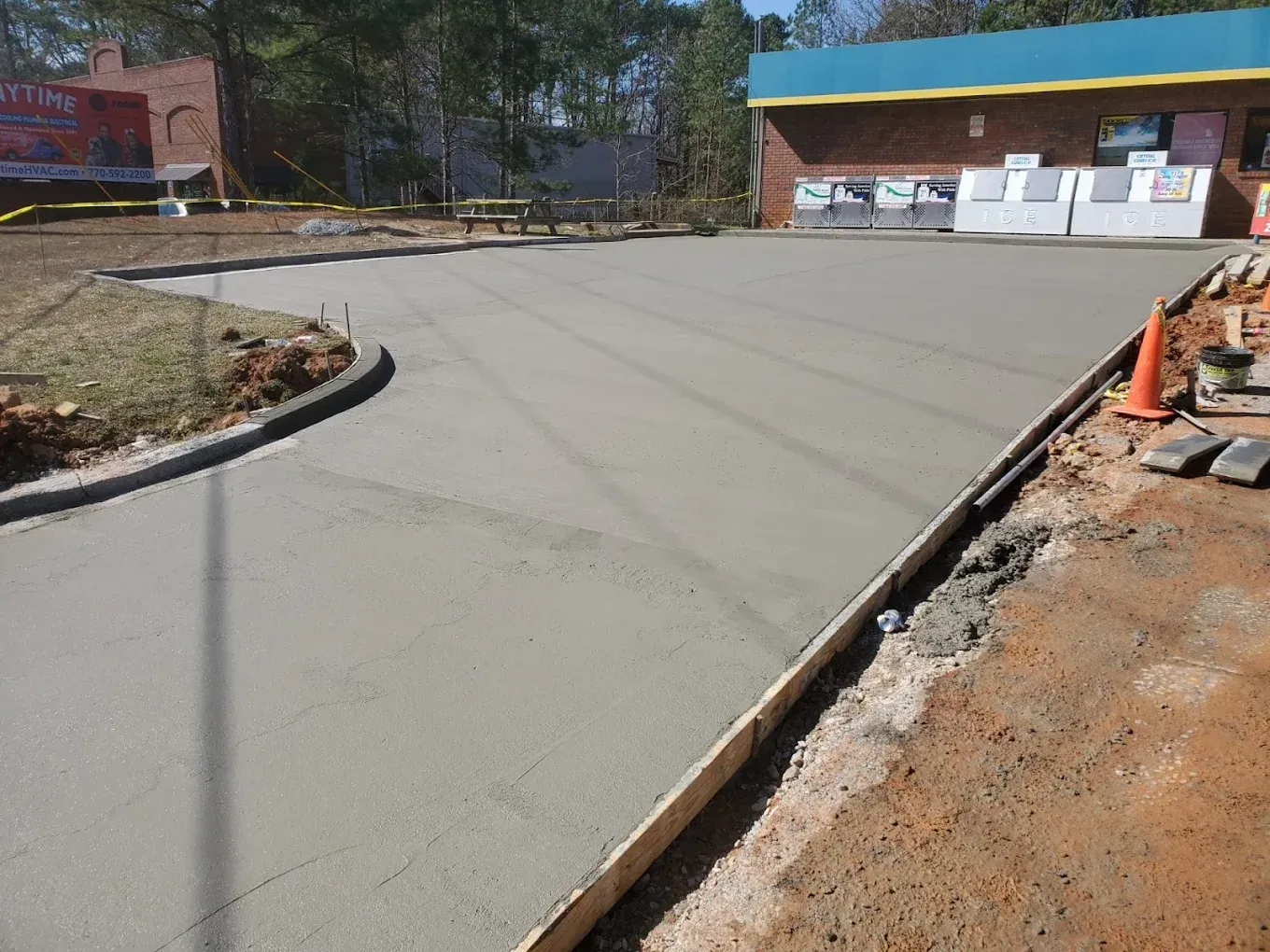 Freshly poured concrete driveway with wooden formwork, next to a building.