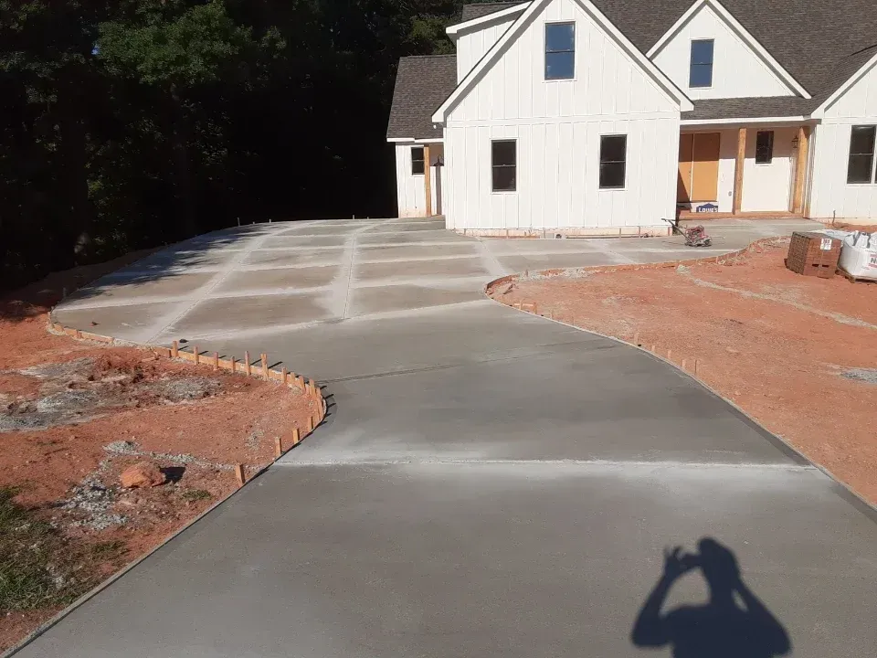 Newly poured concrete driveway with decorative grid design in front of a white house under construction.