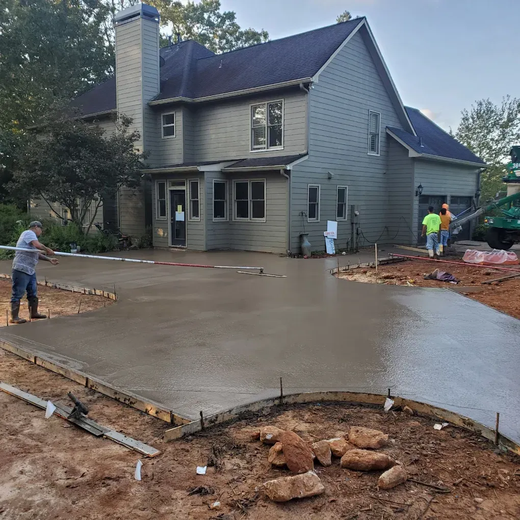 Concrete driveway being poured at a two-story gray house; construction workers in action.
