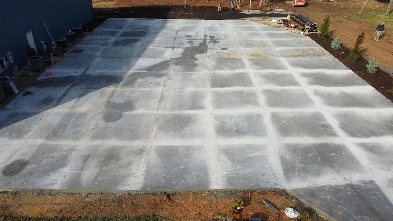 Newly poured concrete slab divided into square sections, outdoors.
