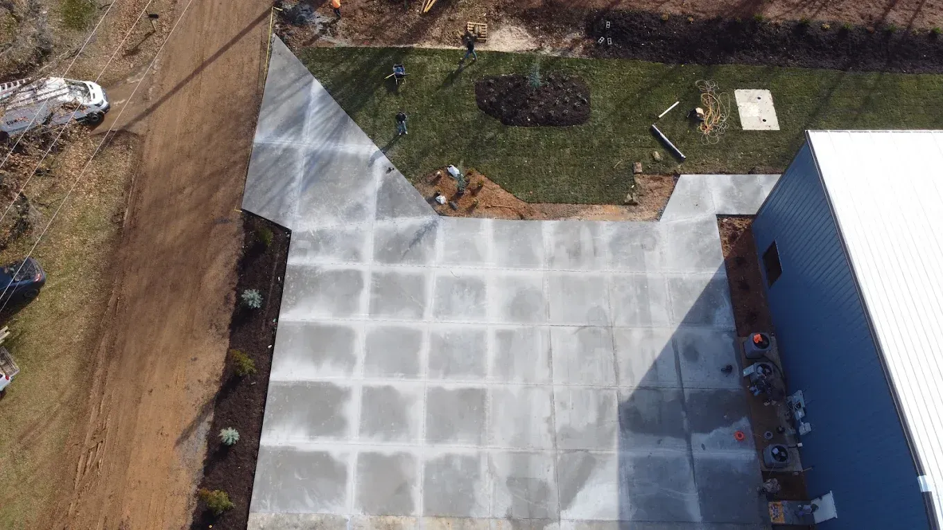 Overhead view of a concrete patio with square grid pattern next to a blue building and grassy area.