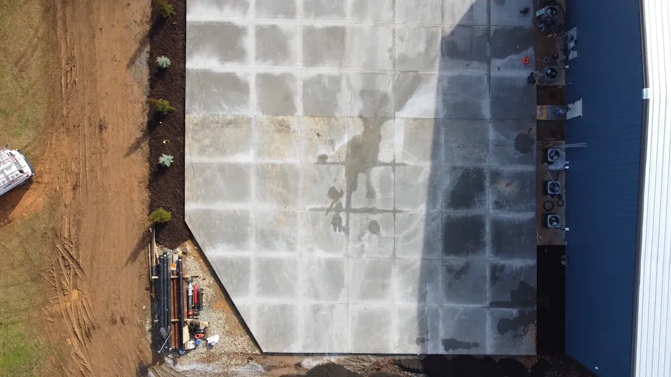Overhead view of freshly poured concrete in a grid pattern beside a building and brown earth.