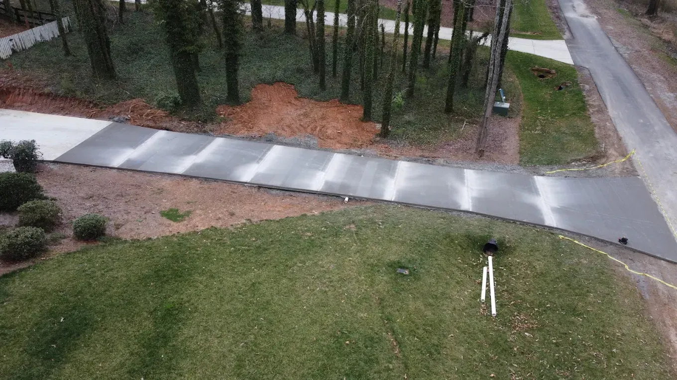 A paved driveway curves through green grass, leading to a wooded area. A road is on the right.