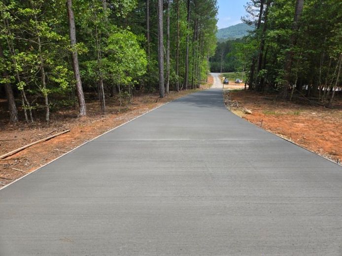 Paved road winding through a forest, leading uphill towards a distant building.