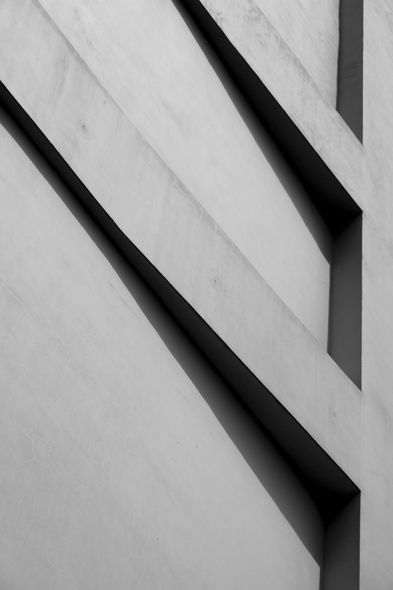 Black and white architectural detail of a concrete wall with angled shadows and recessed linear openings.