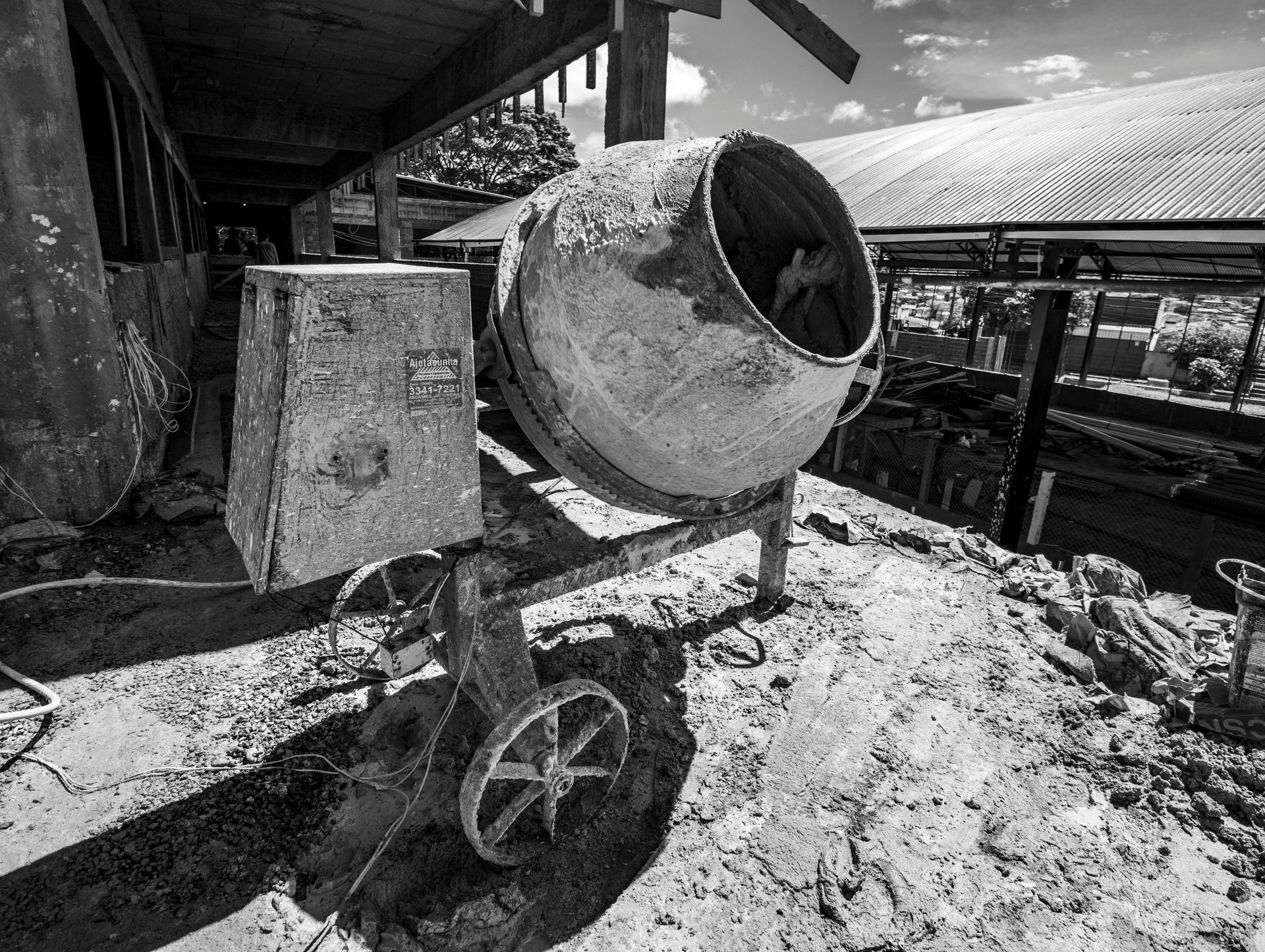 Black and white shot of a concrete mixer, dusty, outdoors, near a building.