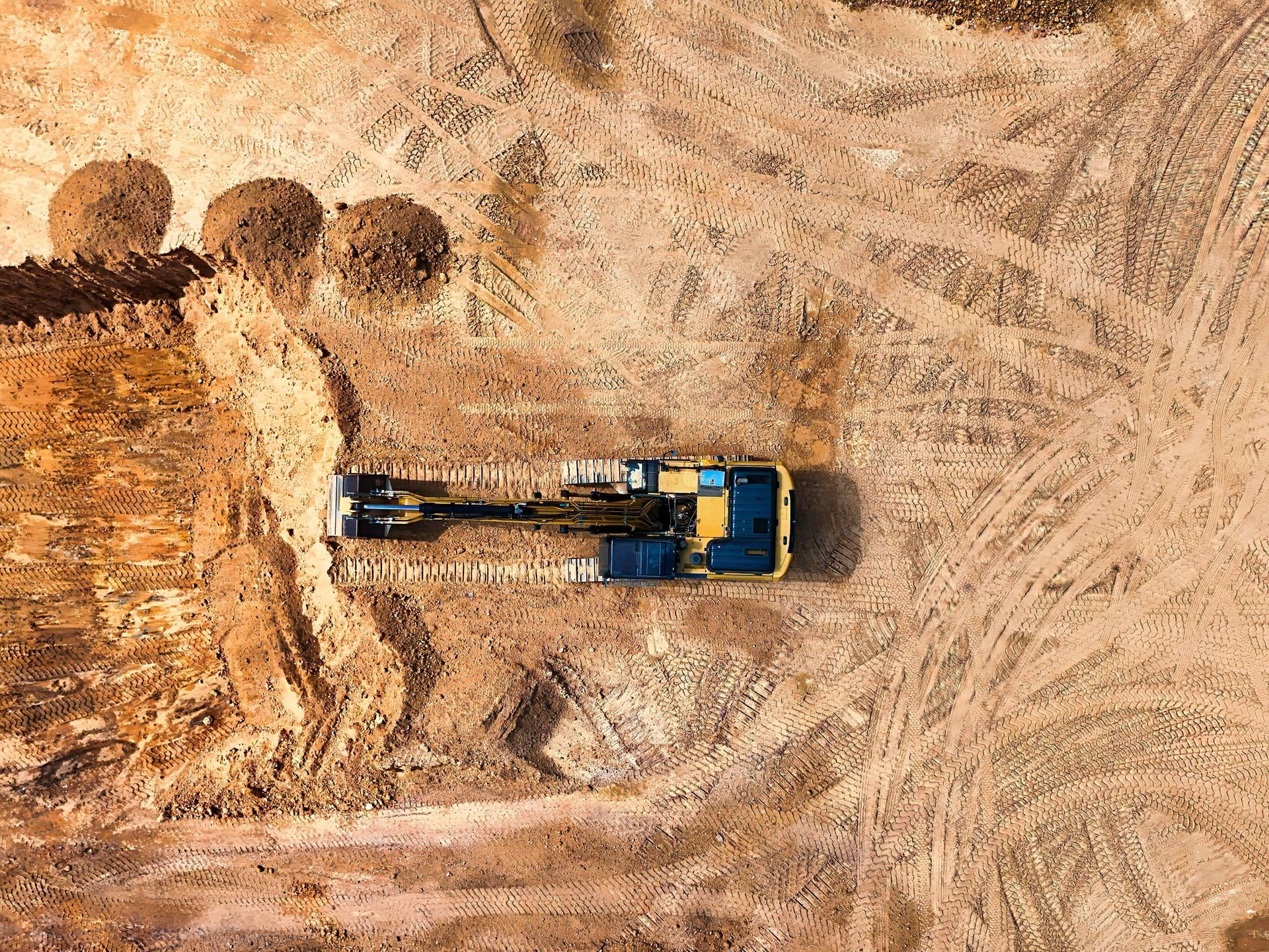 Aerial view: excavator working on a construction site with piles of dirt.