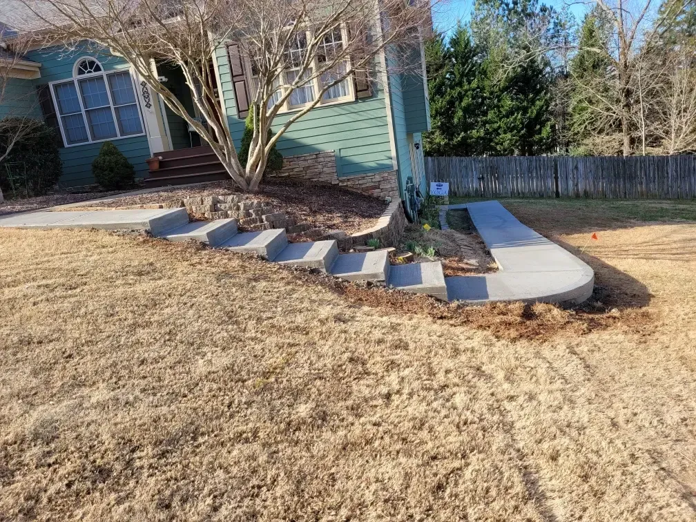 Front yard with concrete steps and curved walkway leading to a house with a small tree in the center.