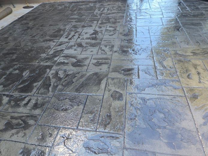 Stamped concrete patio with a stone pattern, dark gray and shiny from a recent seal.