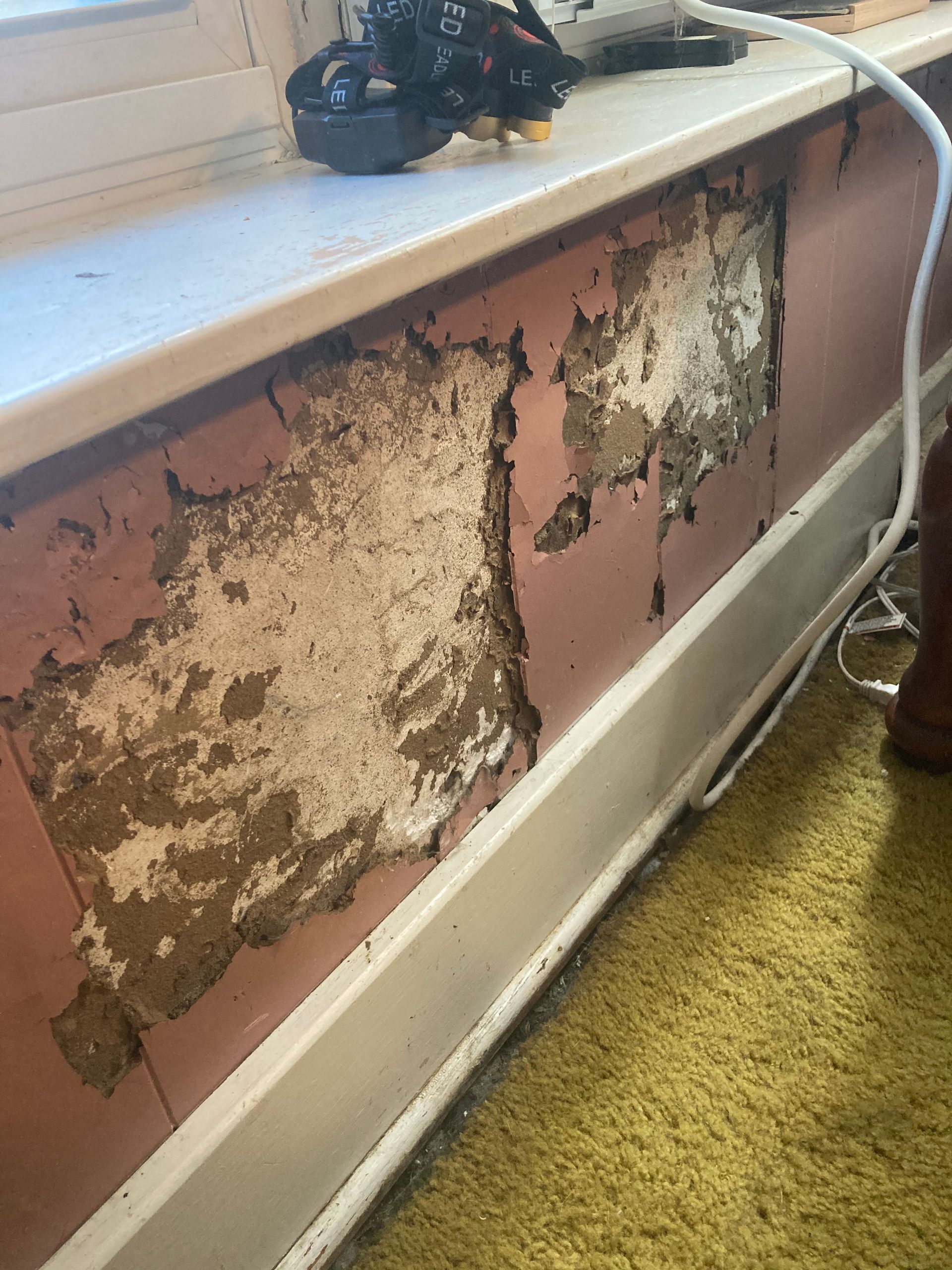 Pink wall with peeling paint below a window sill.