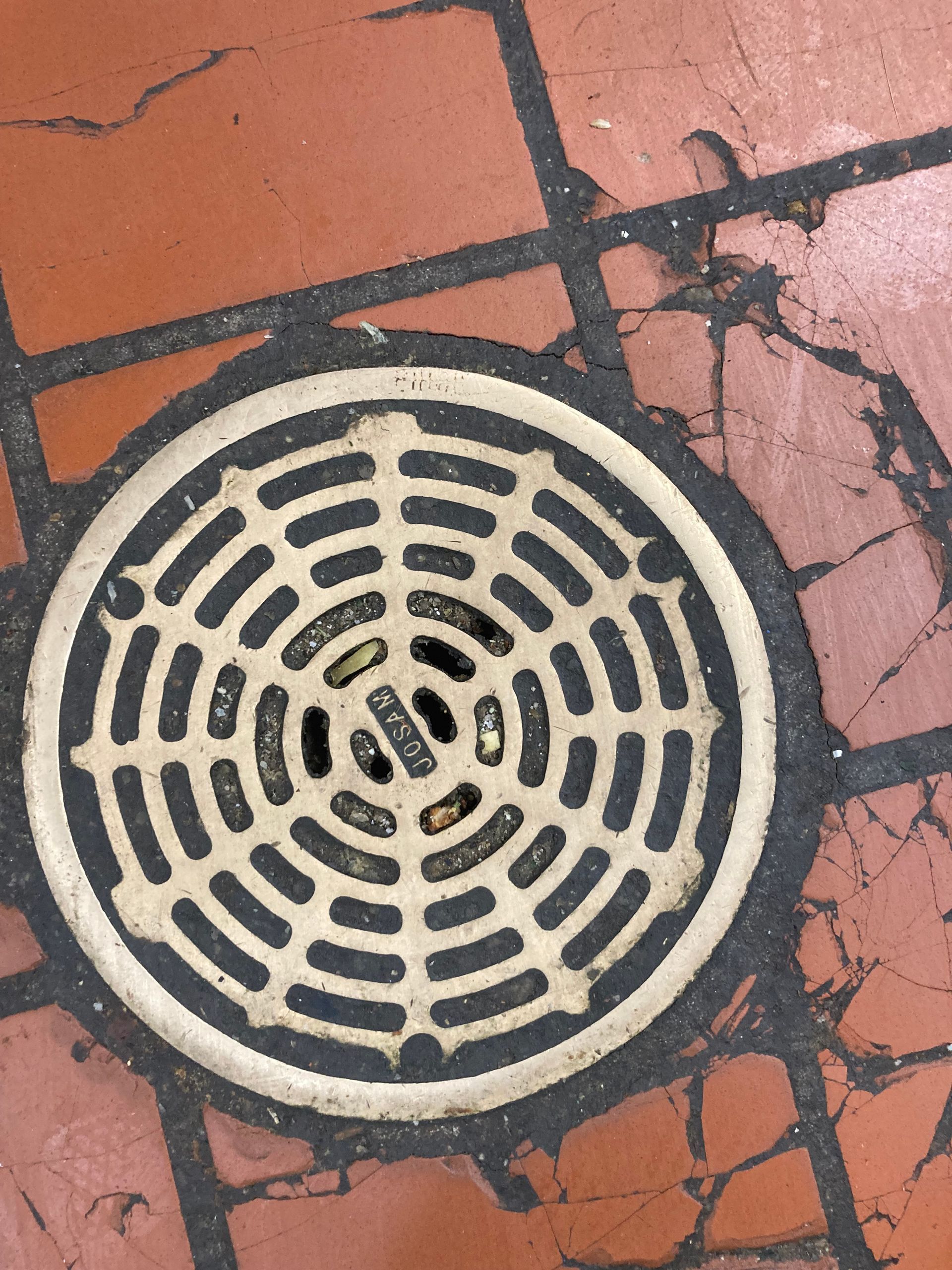 Circular drain cover on red-brown brick. Beige and black detail.