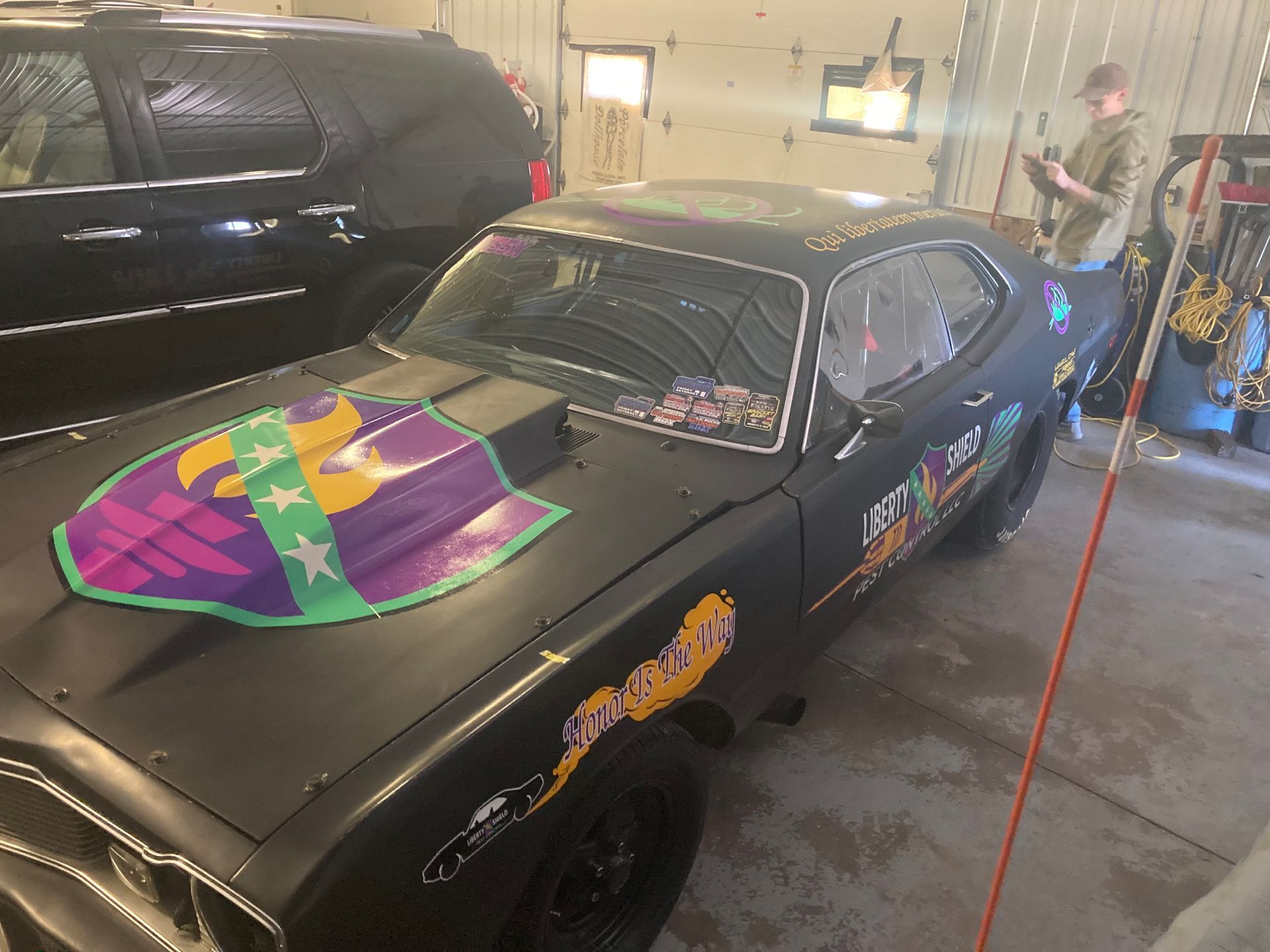 Black muscle car with colorful graphics in a garage; a person stands nearby.