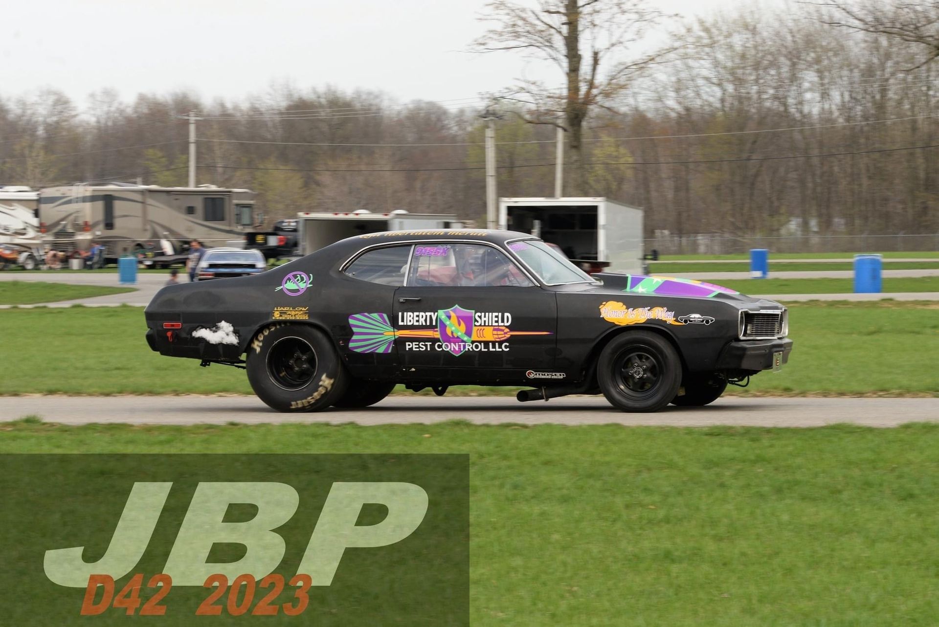 Black race car on a track with colorful graphics. A JBP logo appears in the corner.