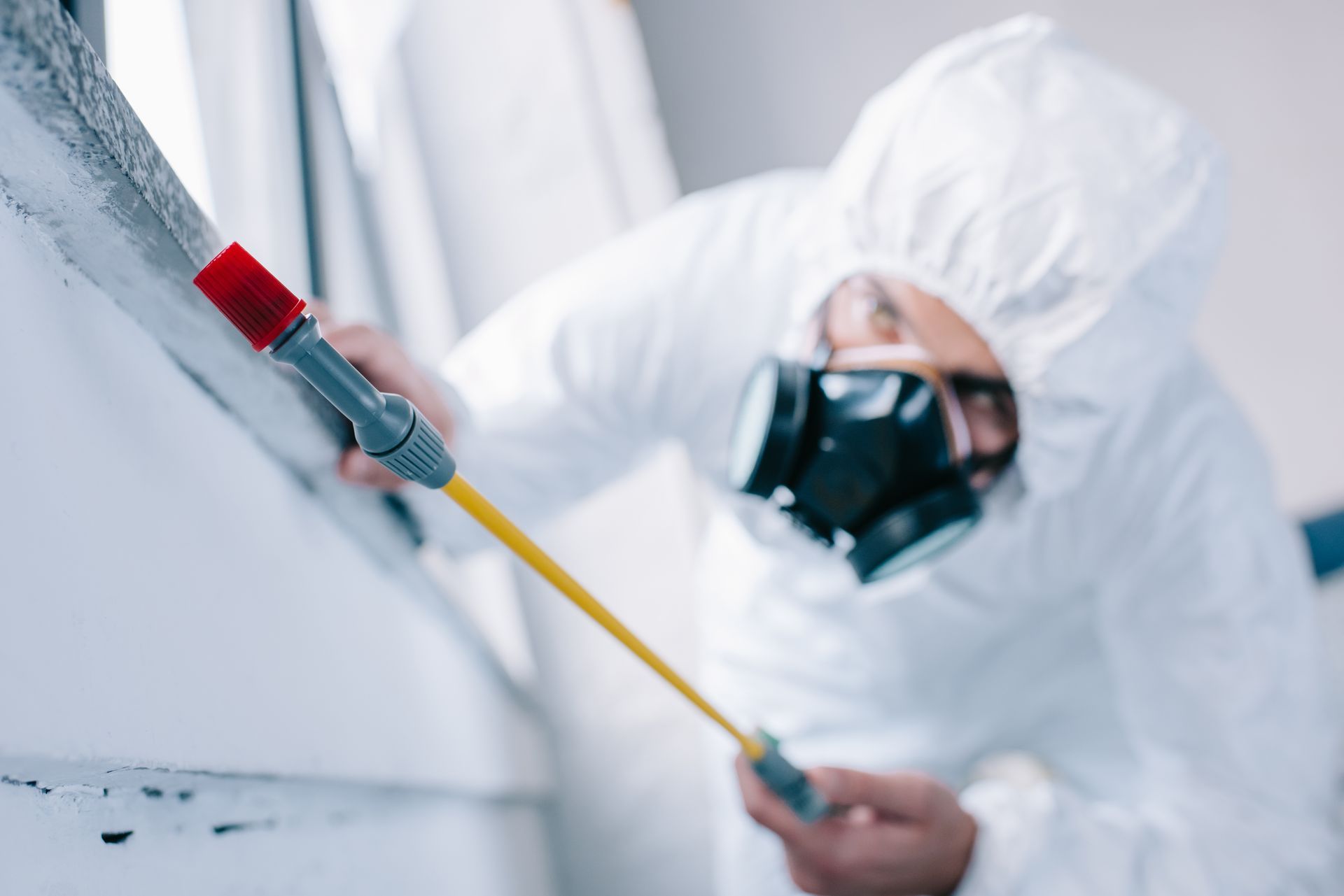 A man in a protective suit is spraying a wall with a sprayer.