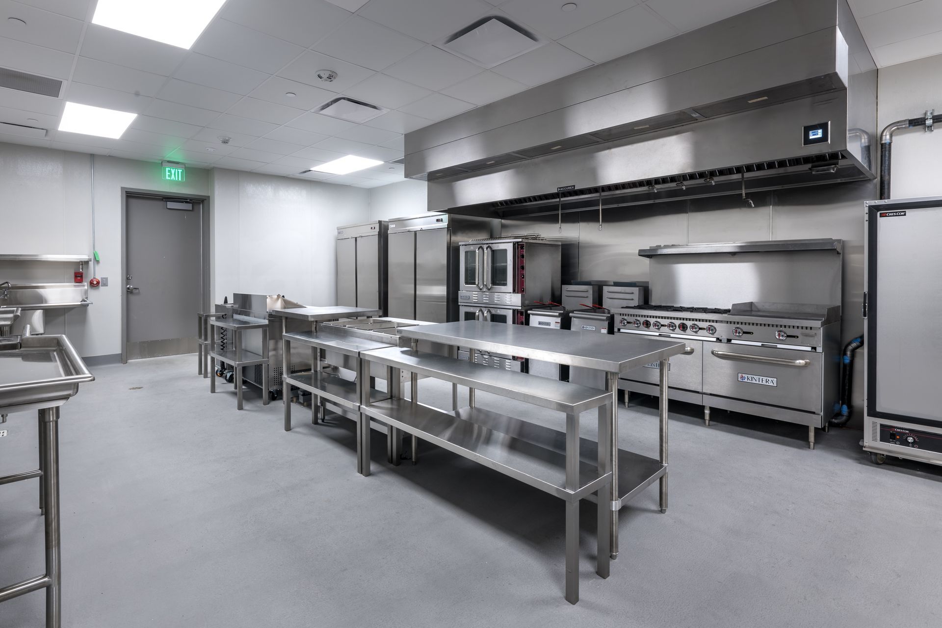 A large kitchen with stainless steel appliances and tables.