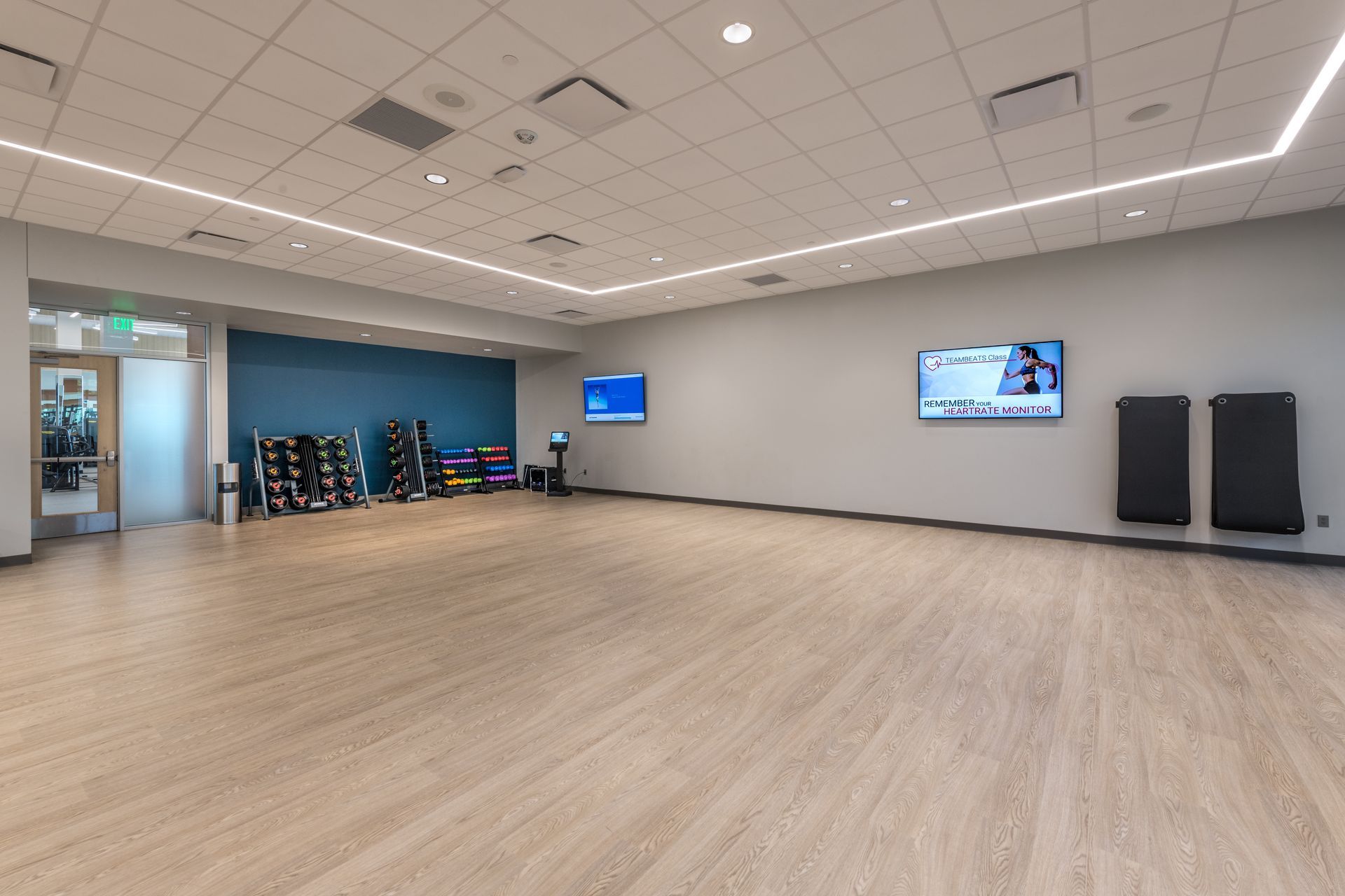 A large empty gym with wooden floors and a television on the wall.