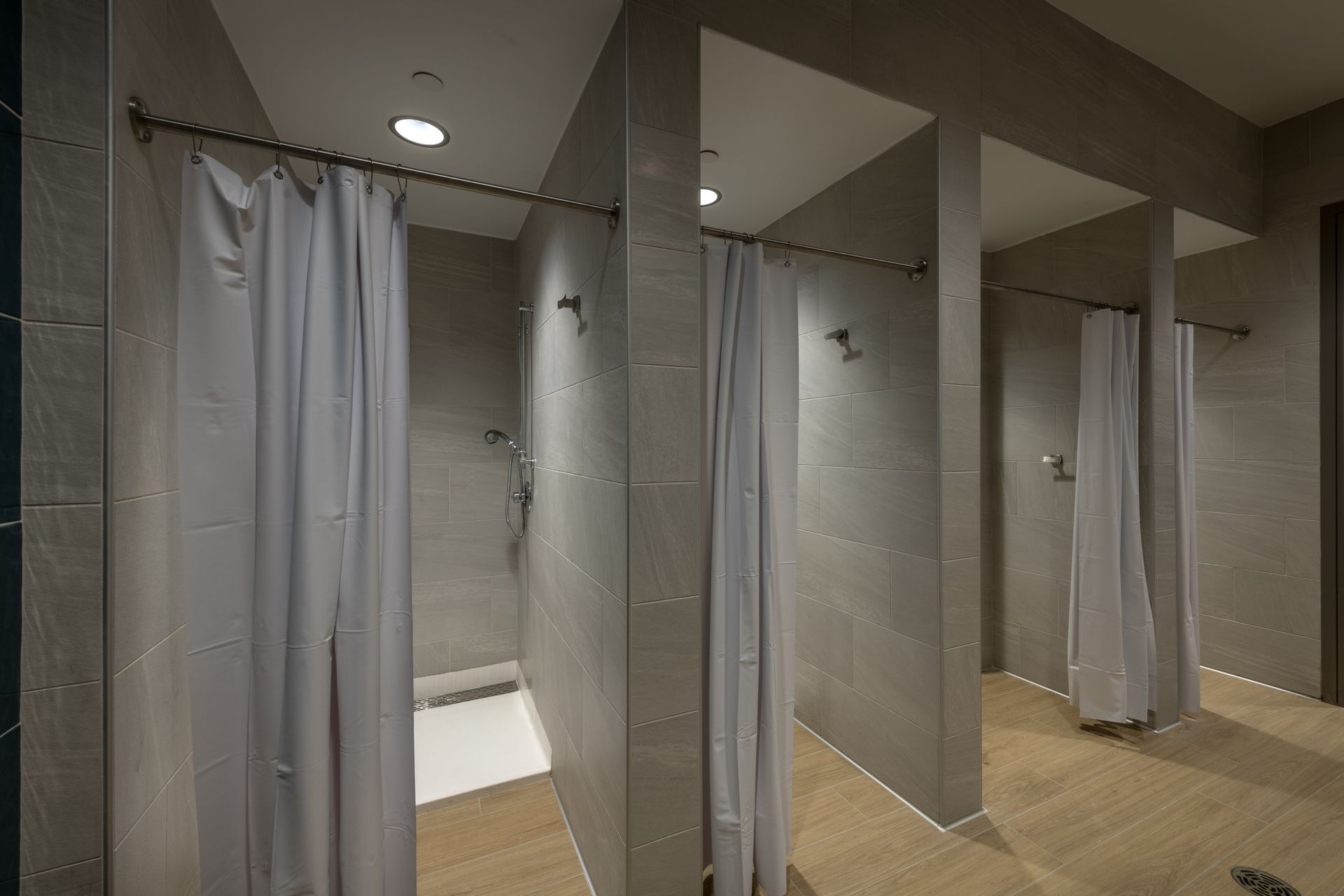 A row of shower stalls with white curtains in a bathroom