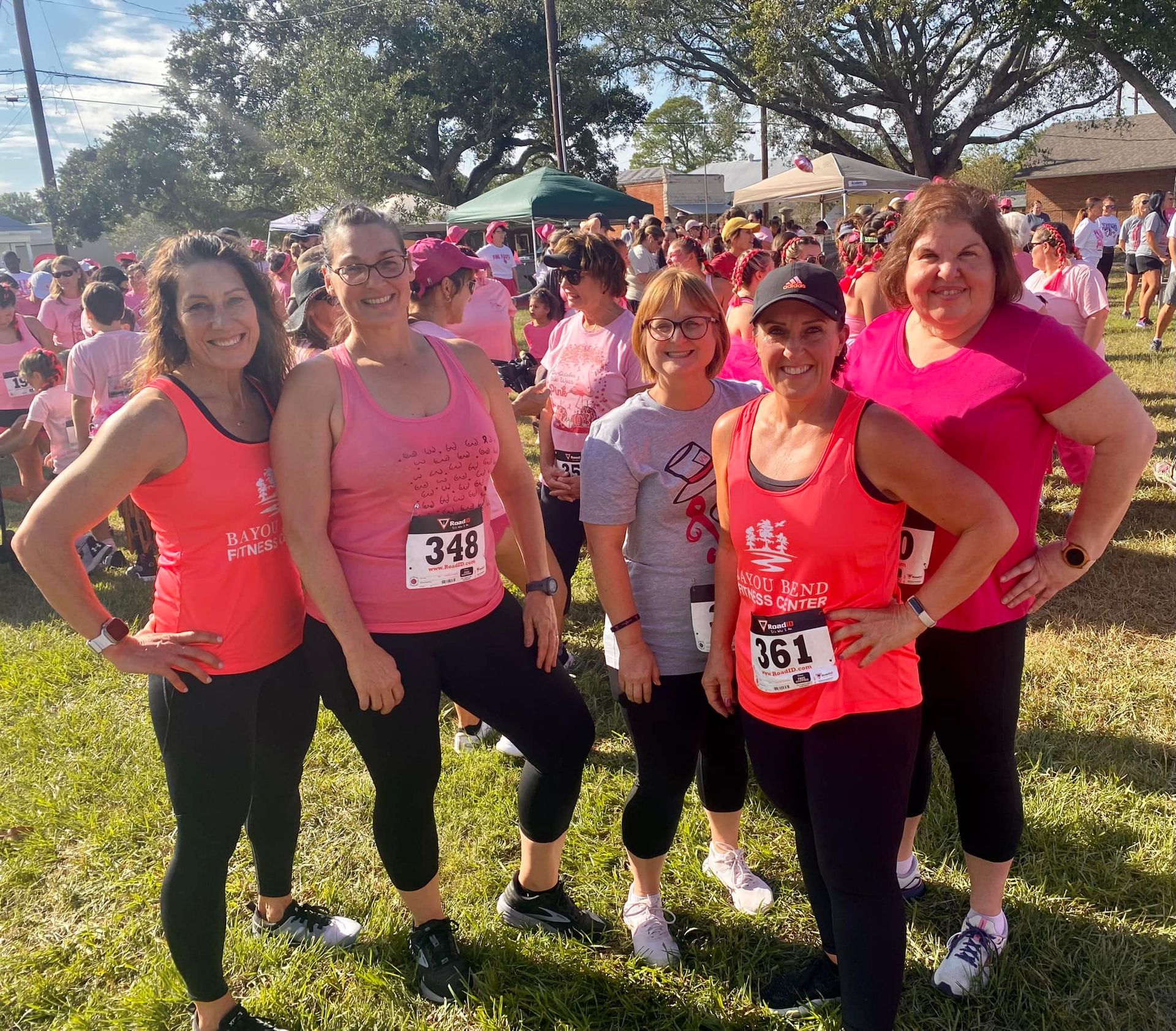 A group of women wearing pink tank tops are posing for a picture.