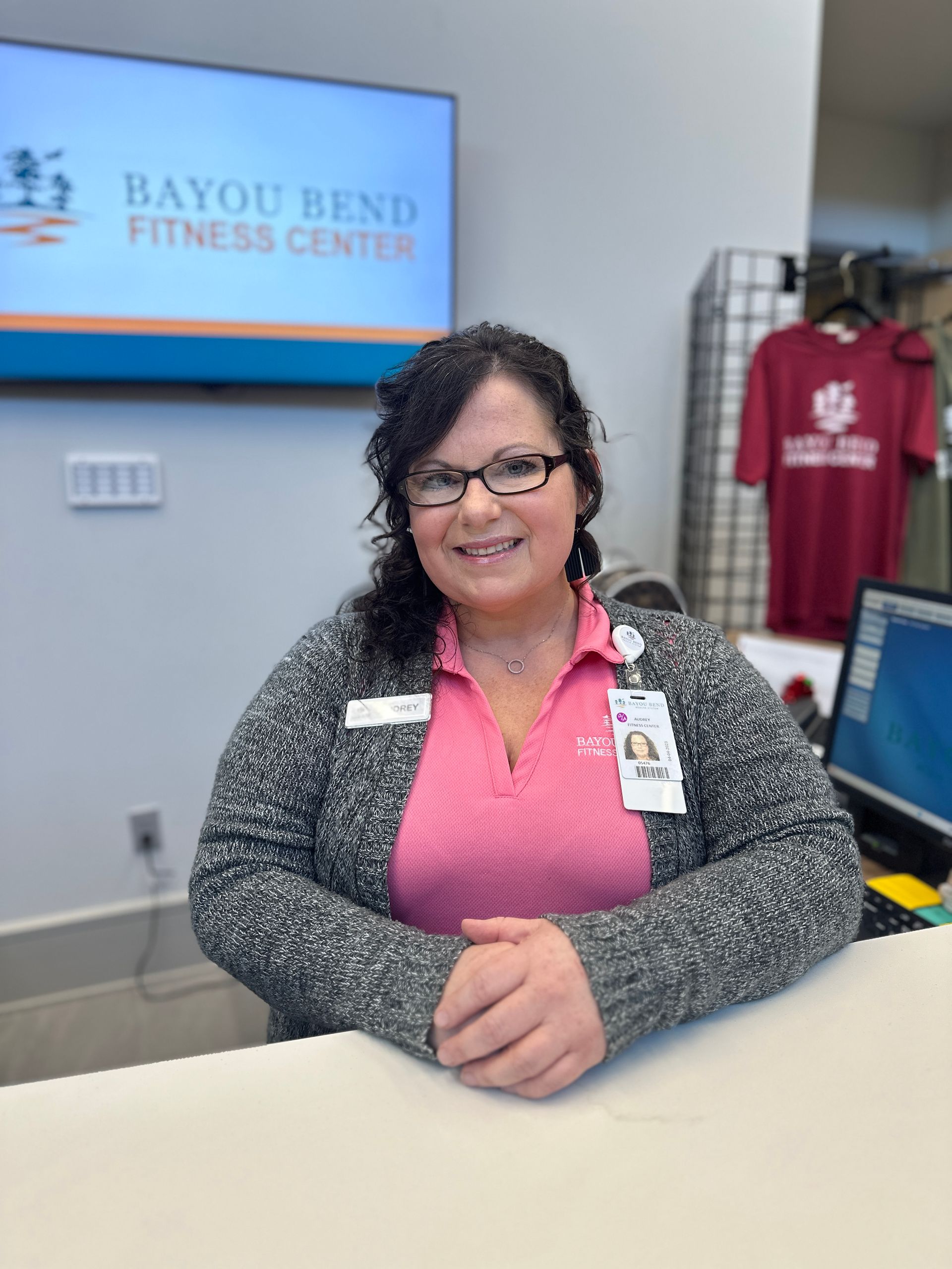 A woman is sitting at a counter in front of a bayou bend fitness center sign.