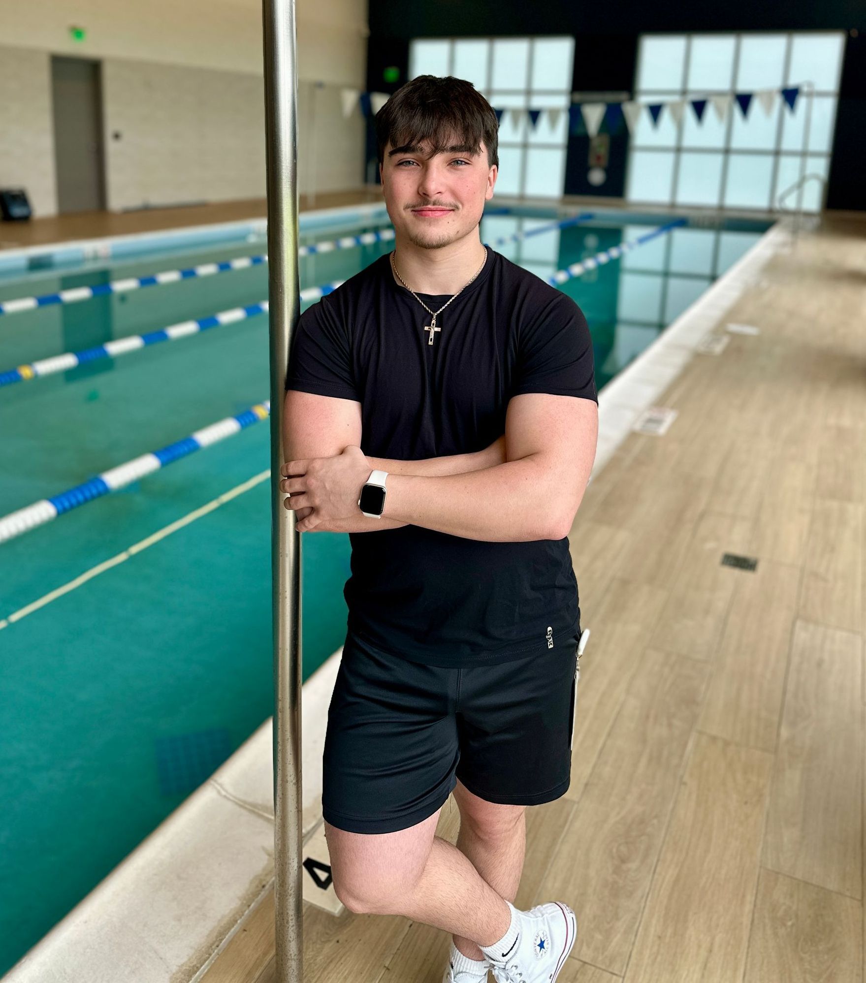 A young man is leaning against a pole in front of a swimming pool.