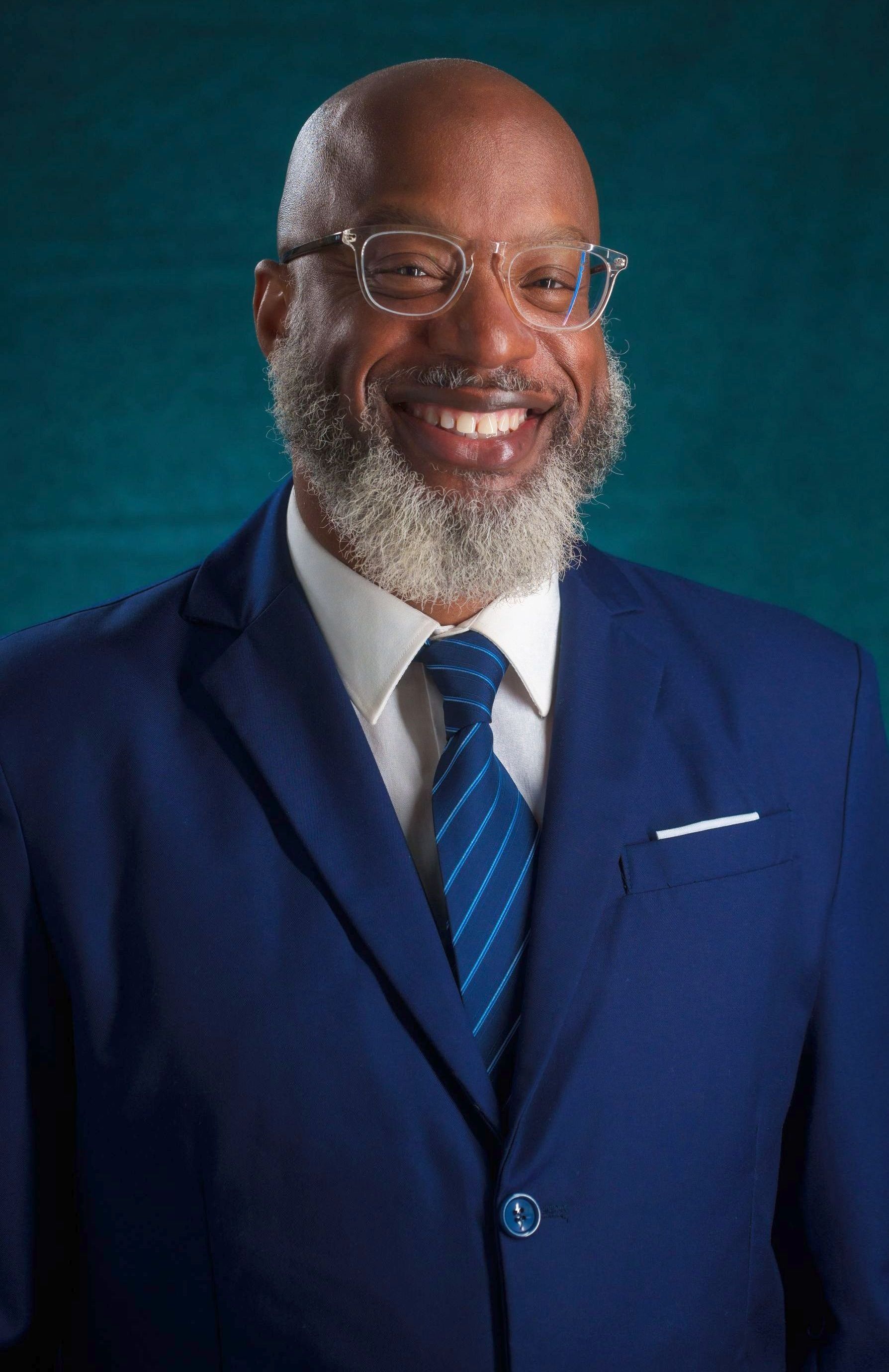 A man with a beard and glasses is wearing a blue suit and tie.