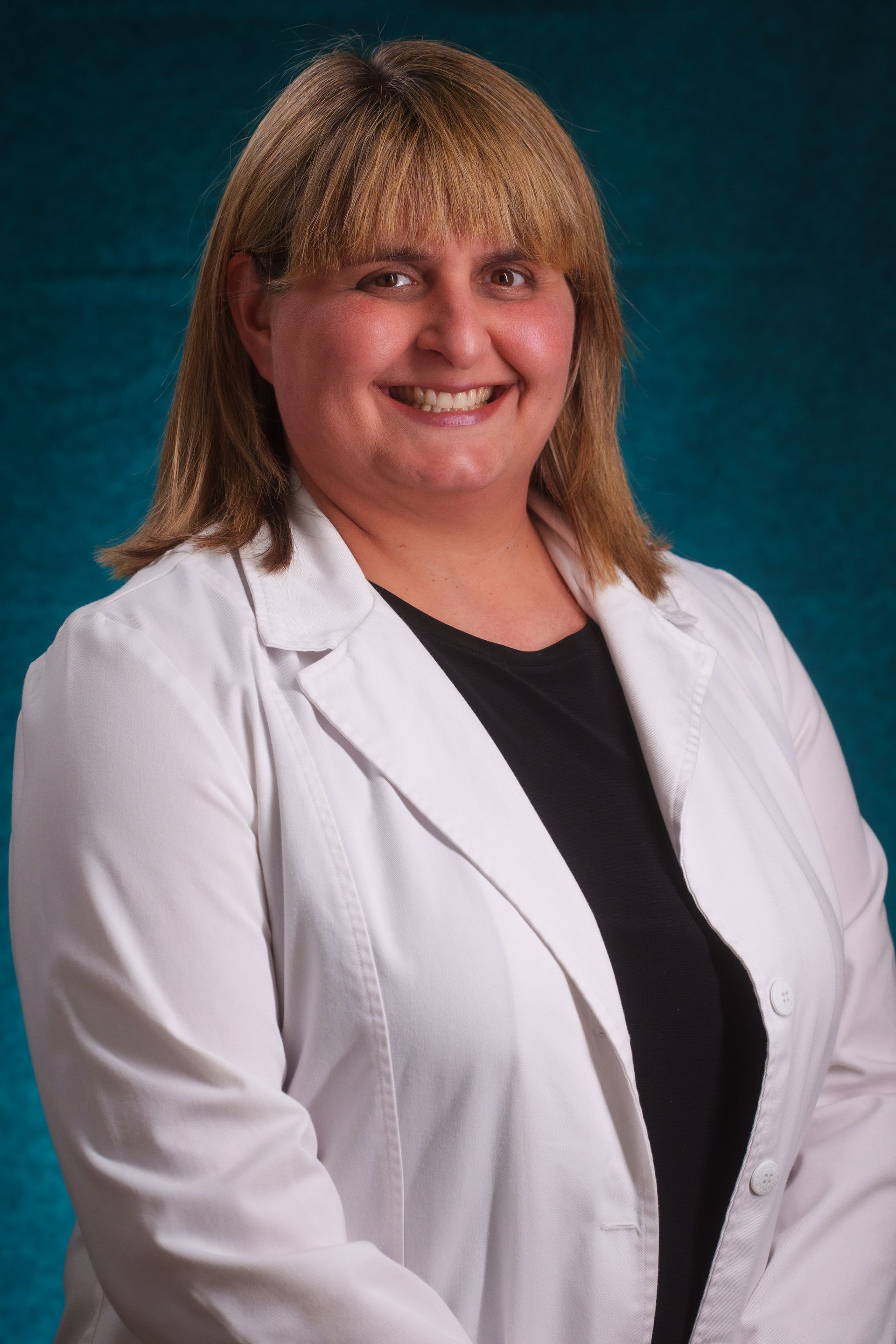 A woman in a white lab coat is smiling for the camera
