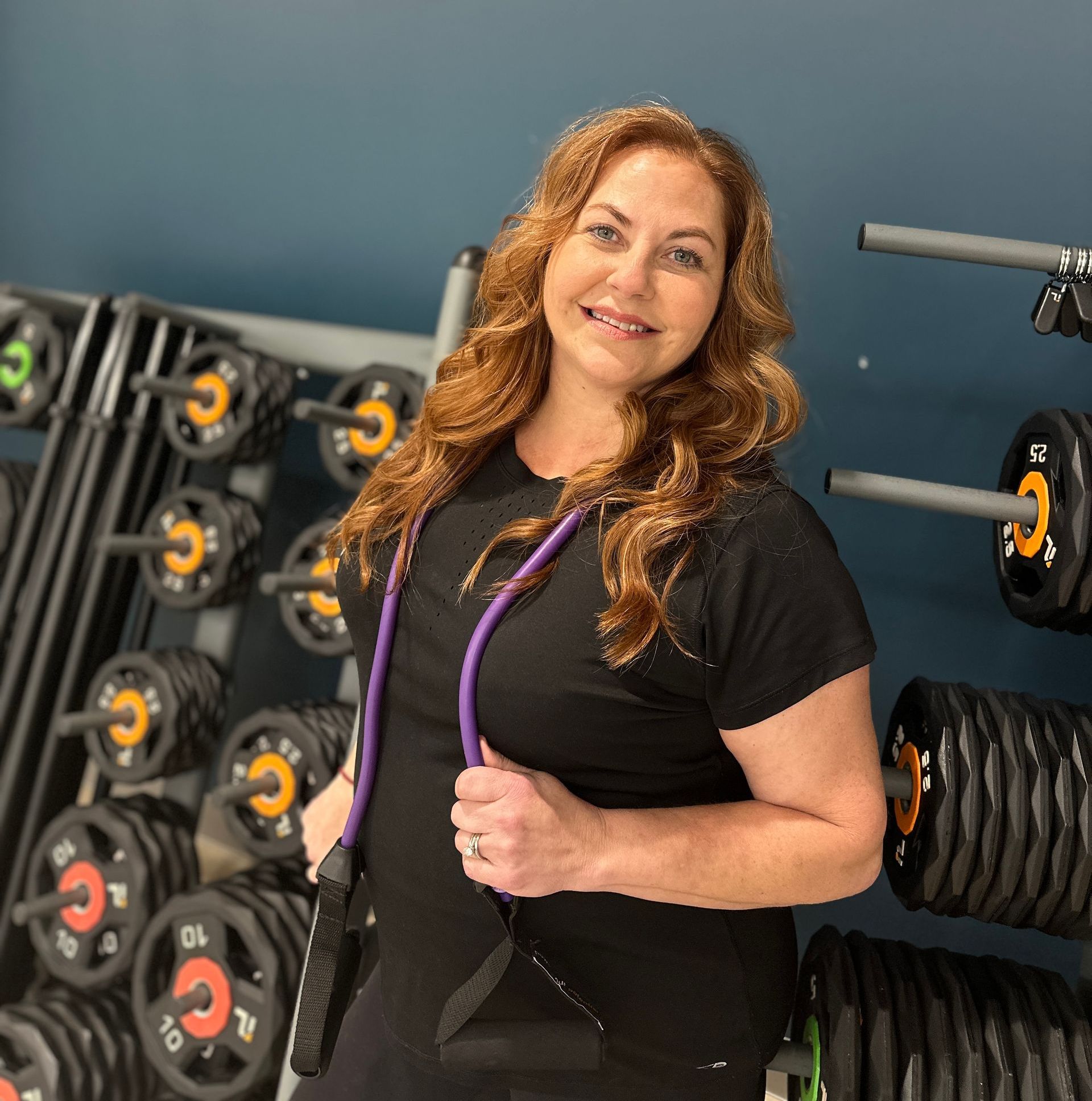 A woman in a black shirt is holding a purple rope in a gym.