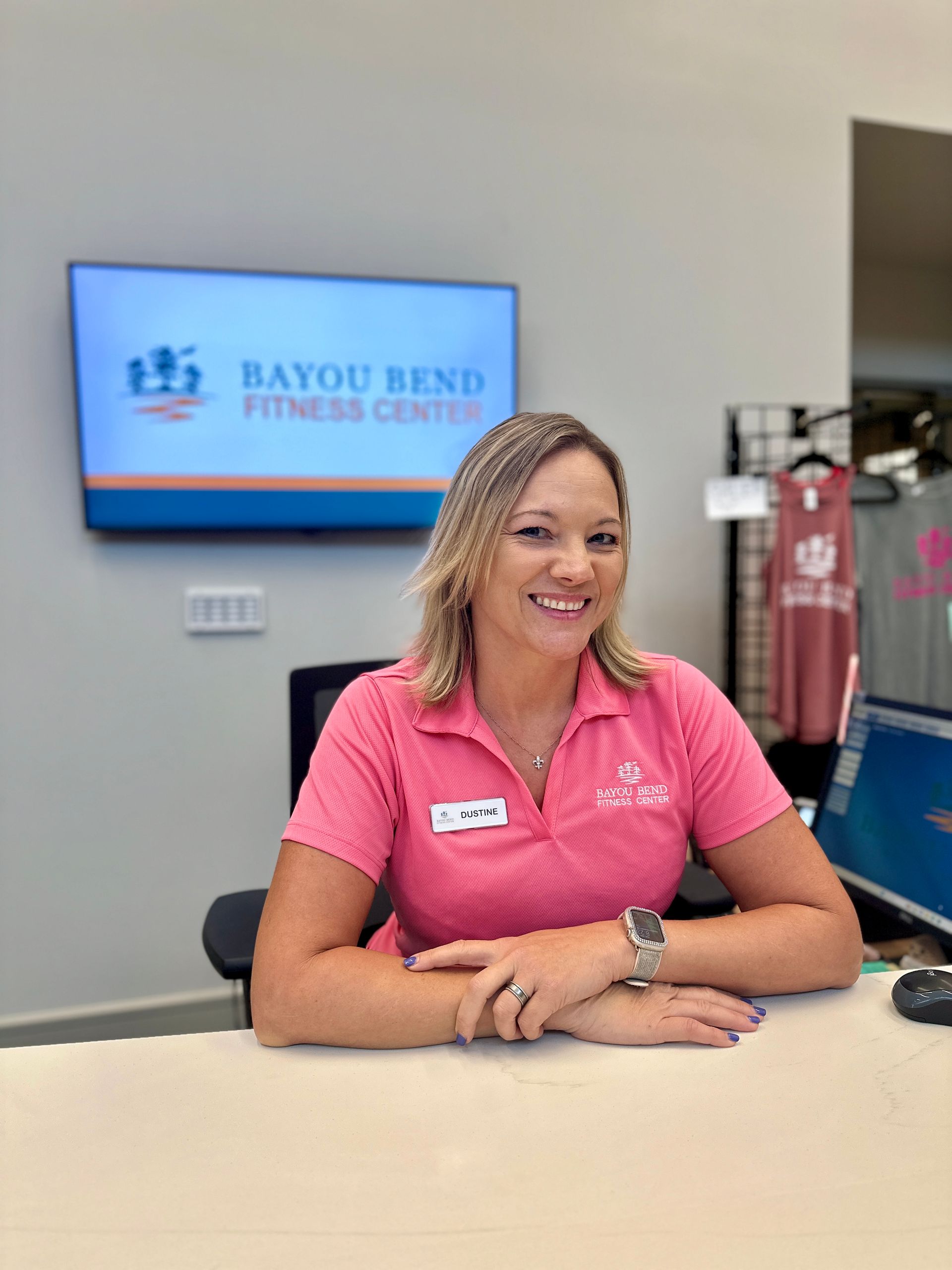 A woman in a pink shirt is sitting at a desk in front of a television.