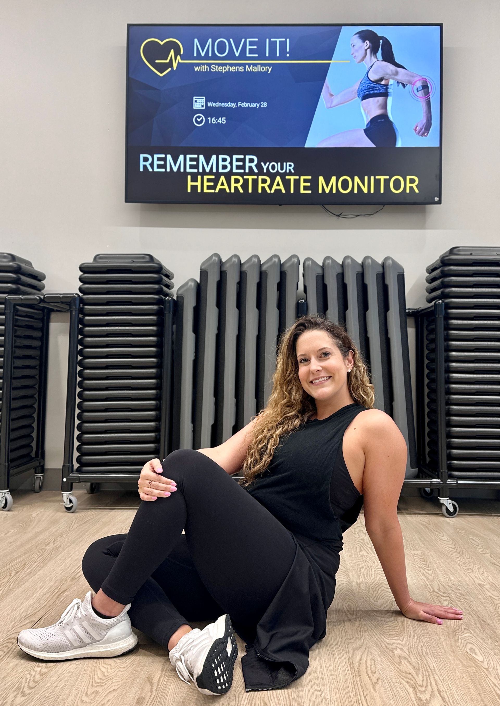 A woman is sitting on the floor in front of a monitor.